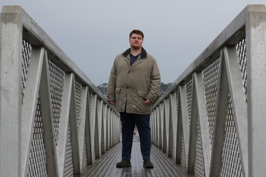 Sean Wendes stands on an industrial looking bridge in George Town. The weather is overcast.