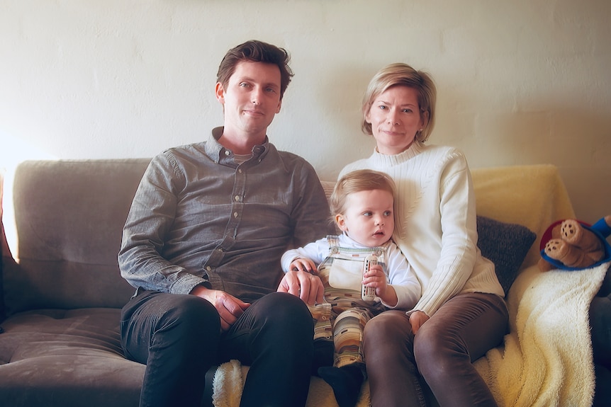 A man, a woman and their toddler son sit on a couch.