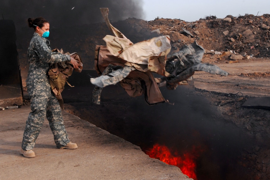 Equipment manager tossing uniform items into a burn pit.