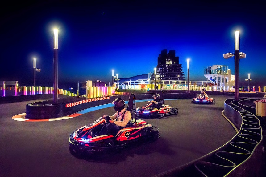 Cruise passengers take part in a go-kart race on the open water at night.