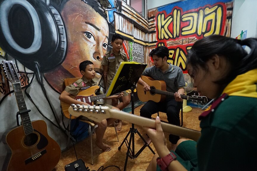 A man teaches teenagers how to play guitars.