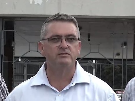 A man wearing glasses and a white shirt speaks outside a building.