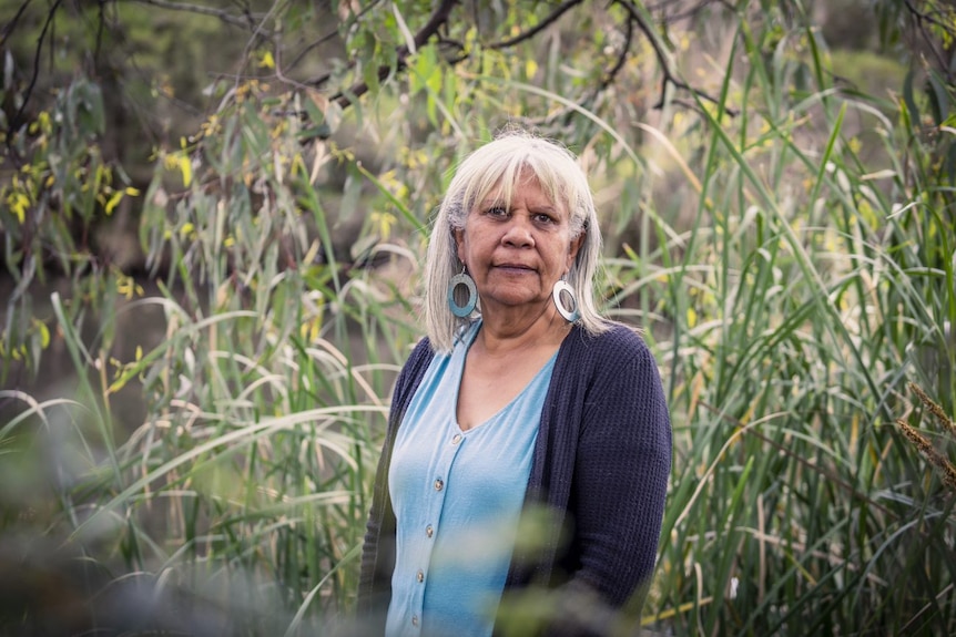 Aunty Eva Jo Edwards surrounded by vegetation, looking towards the camera