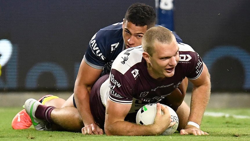 A Manly NRL player lies on the ground with the ball beneath him after he scored a try.