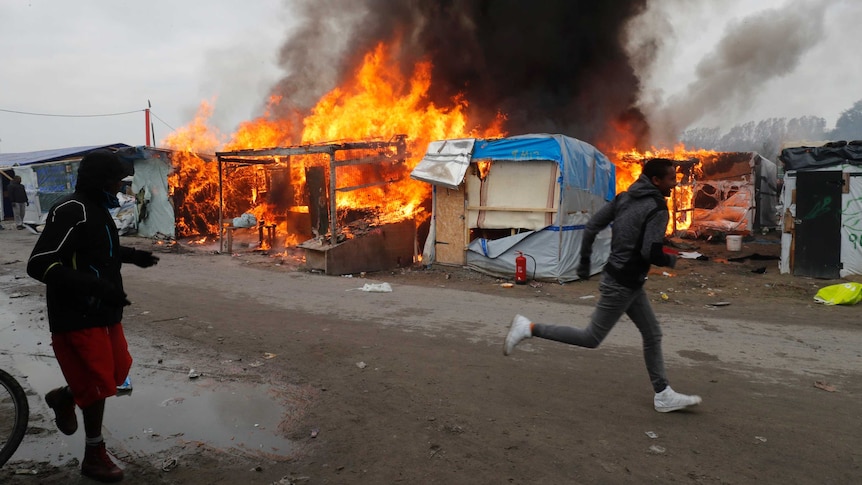 Two men run past burning makeshift shelters