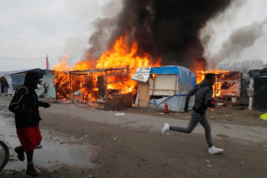 Two men run past burning makeshift shelters