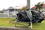 Black trampoline, frame badly twisted, out the front of a house