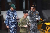 Three defence force personnel, including someone from the Air Force, walk with takeaway coffee cups.