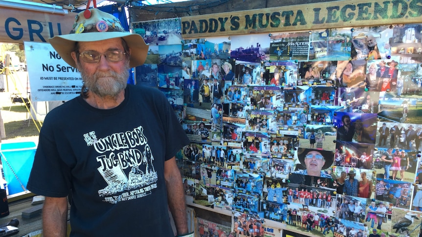 Older man stands with floppy akubra hat in front of lots of photos and sign saying Paddy's Musta Legends.
