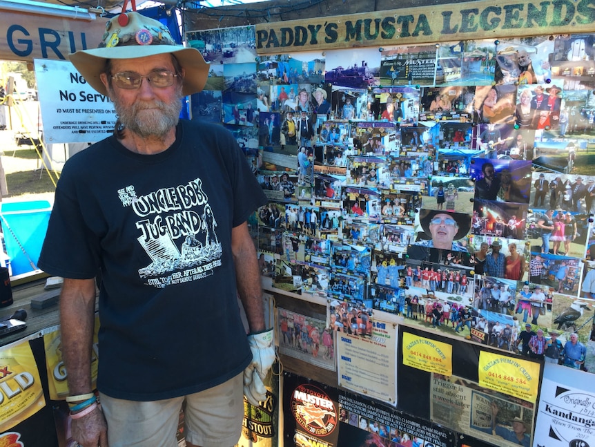 Older man stands with floppy akubra hat in front of lots of photos and sign saying Paddy's Musta Legends.