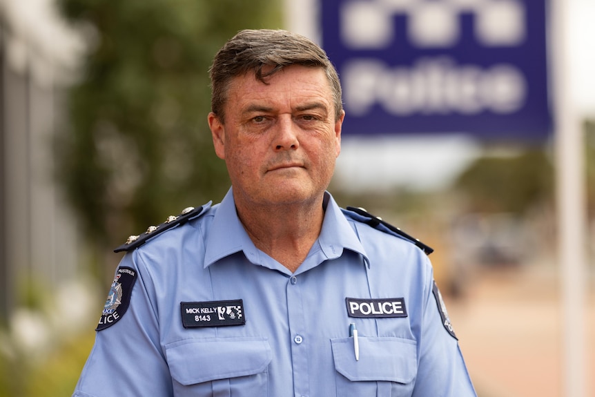 A mid-shot of WA Police Inspector Mick Kelly posing for a photo outside a police station with a serious look on his face.