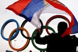 A person, with back to camera, holds a Russia flag above their head. The Olympic rings are behind him.