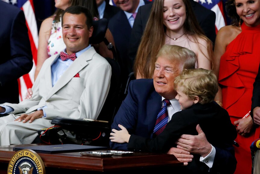 A seven-year-old boy hugs Donald Trump, who has an awkward look on his face.