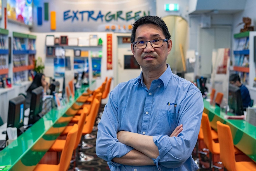 A middle aged man stands with his arms crossed in an empty travel agency