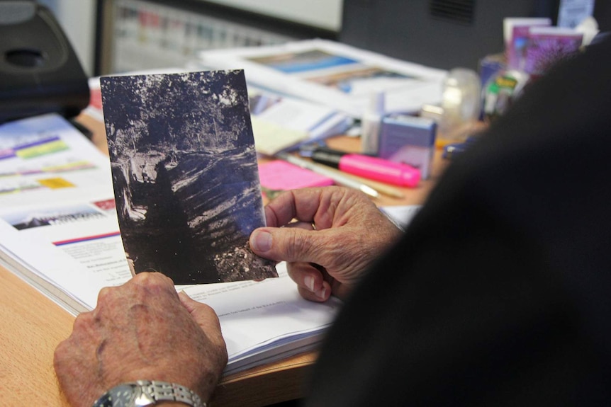 A photo of Norman Cramp holding an archival photo of people in trenches.