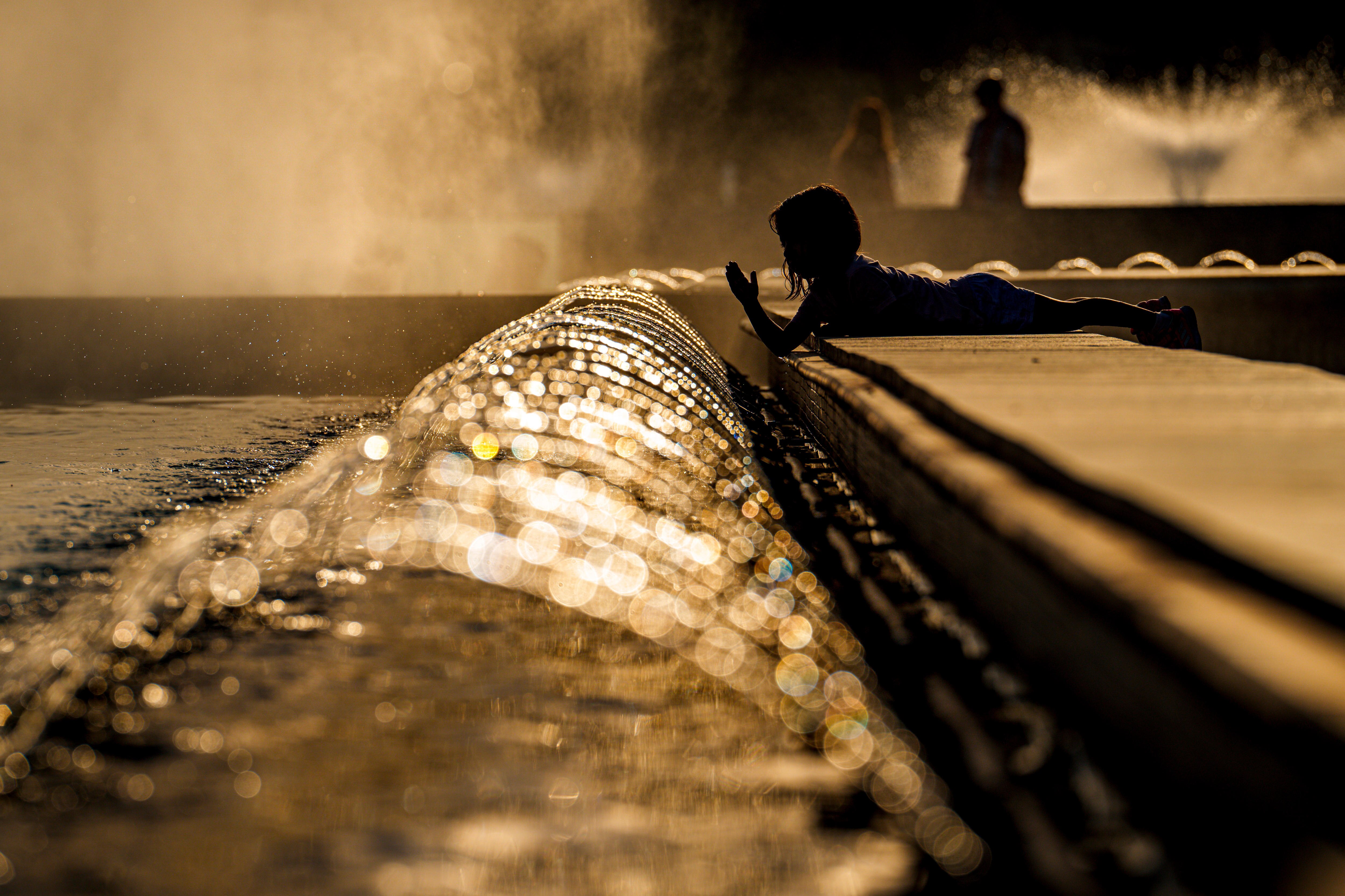 Cerca de una fuente durante la puesta de sol.  Al fondo juega una niña. 