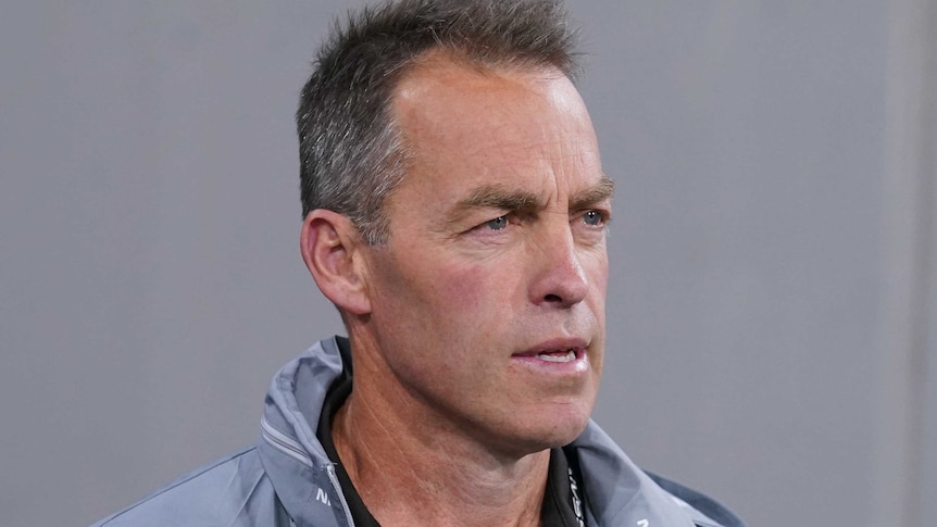 Alastair Clarkson wears a grey jacket and looks pensive