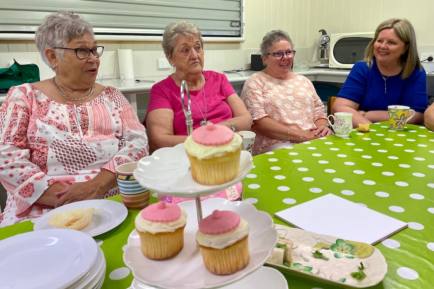 four women sit at a table chatting with cupcakes decorated like breasts in the foreground