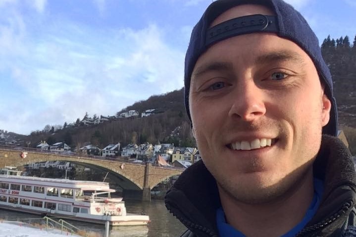 A man in a hat takes a selfie in front of a river