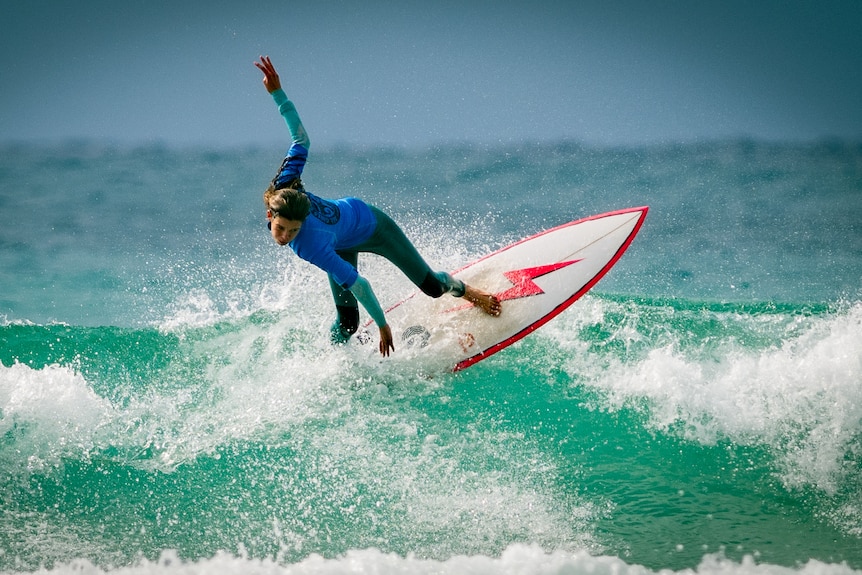 A teenage girl in the surf mid-wave. Her board has a bright red lightning bolt on it