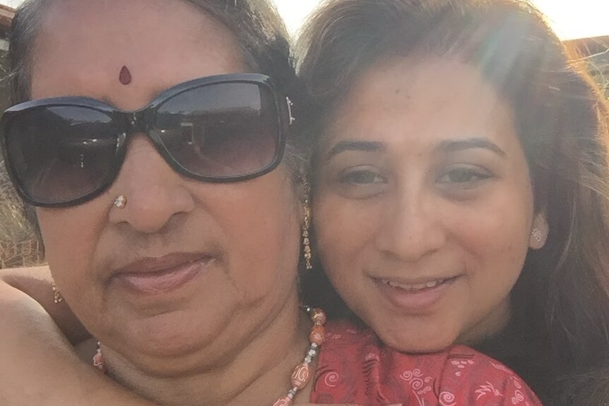 Photo of elderly and younger woman hugging, both smiling and facing camera, with sun streaming into photo from above.