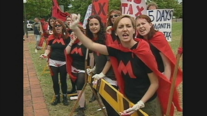 Archival footage of a protest against cabinet ministers in 2000 shows early opposition to having the GST applied to women's sanitary items