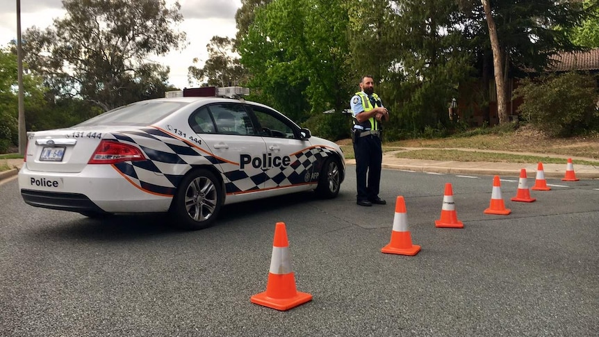 An officer and car next to a line of traffic cones blocking the road.