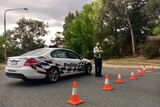 An officer and car next to a line of traffic cones blocking the road.