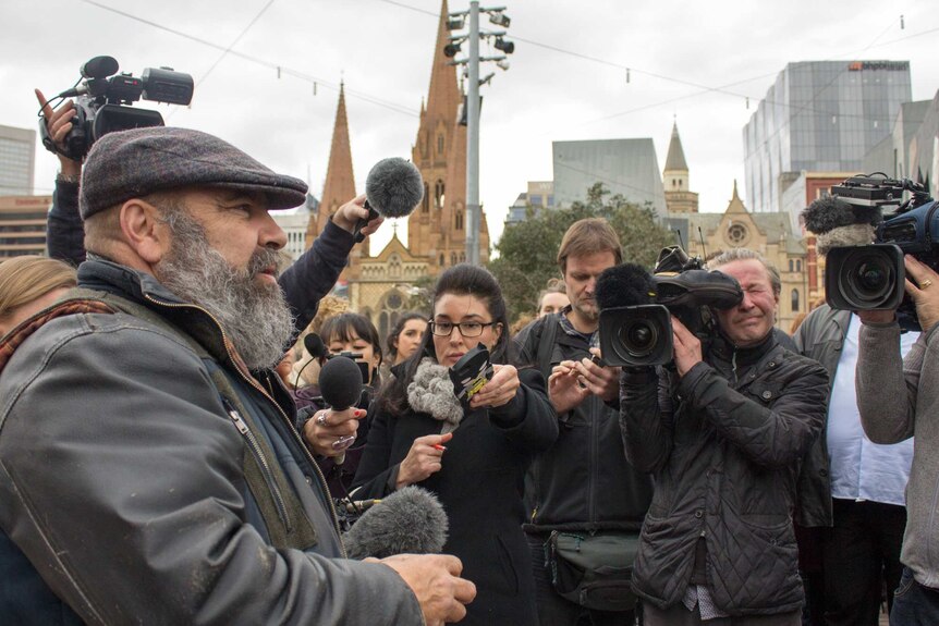 A man speaks, surrounded by media