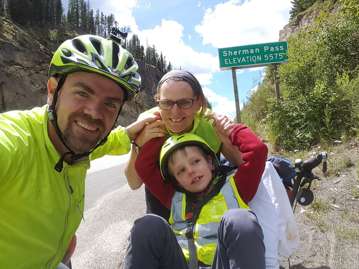 Fiona Churchman, Travis Saunders and their son Patch in front of a road sign saying Sherman Pass