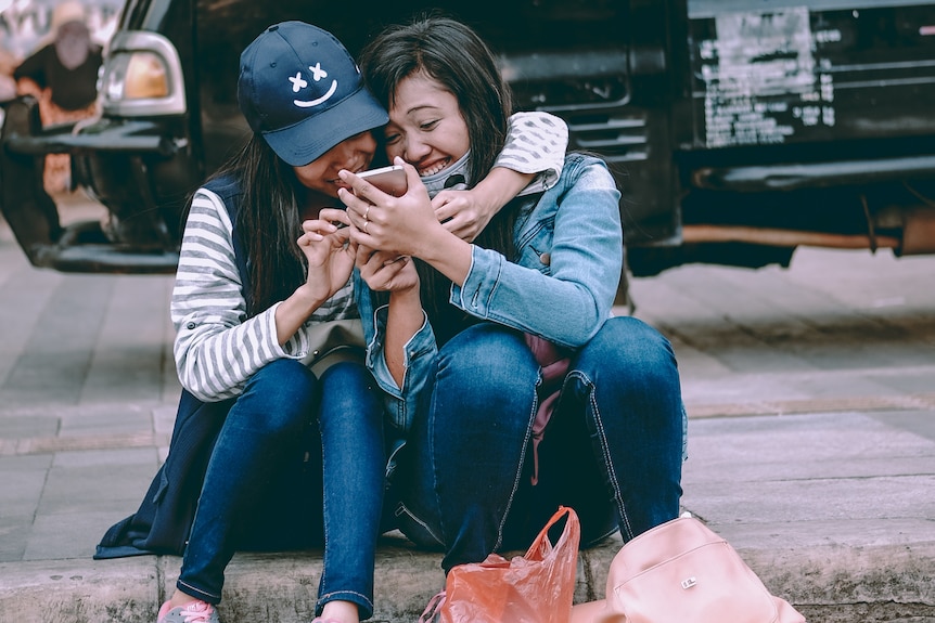 Two women sitting on the pavement with their arms around each other