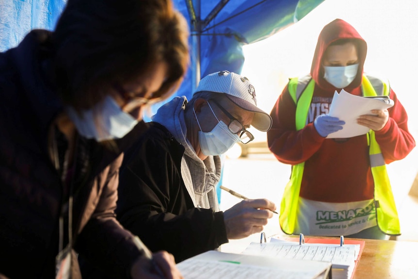 People in face masks examining ballots