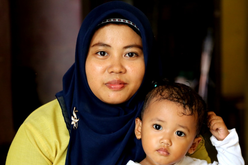 A woman in a hijab holds a toddler in her arms.