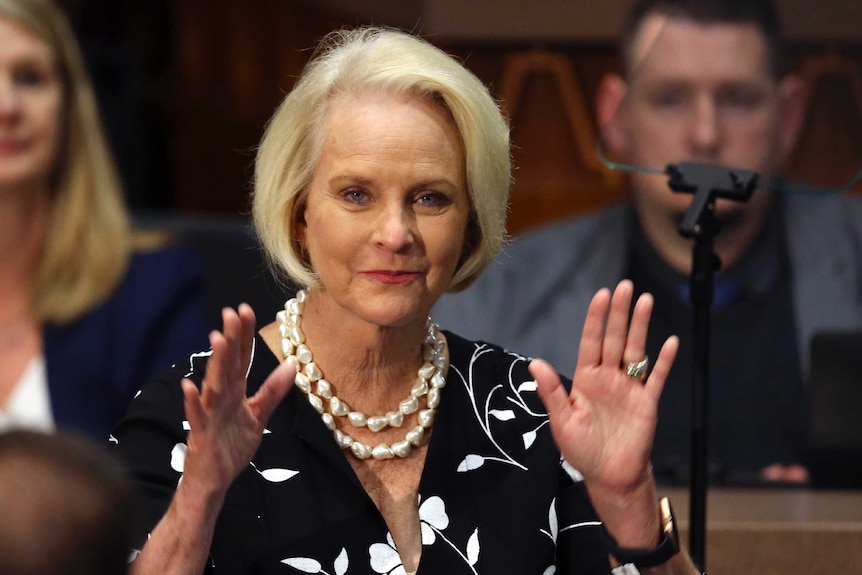 Cindy McCain with blonde hair and pearls gestures with two hands.