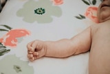 Baby lying in a cot with patterned floral sheet