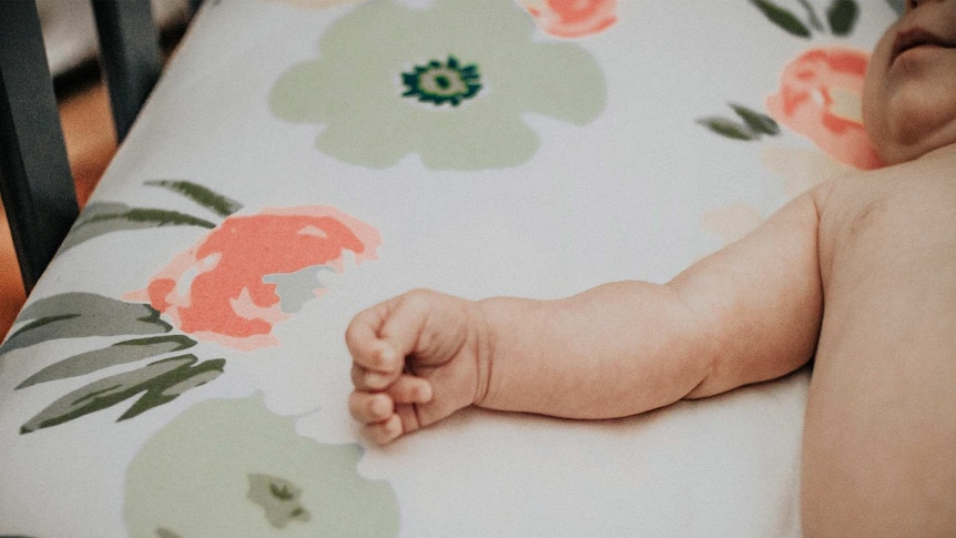 Baby lying in a cot with patterned floral sheet