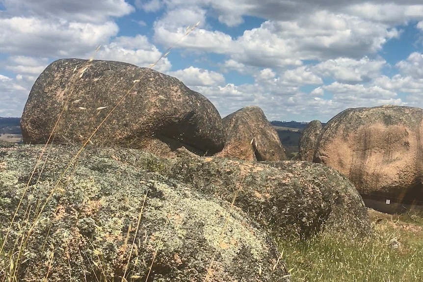 Large boulders on a hill side with rural land in the background