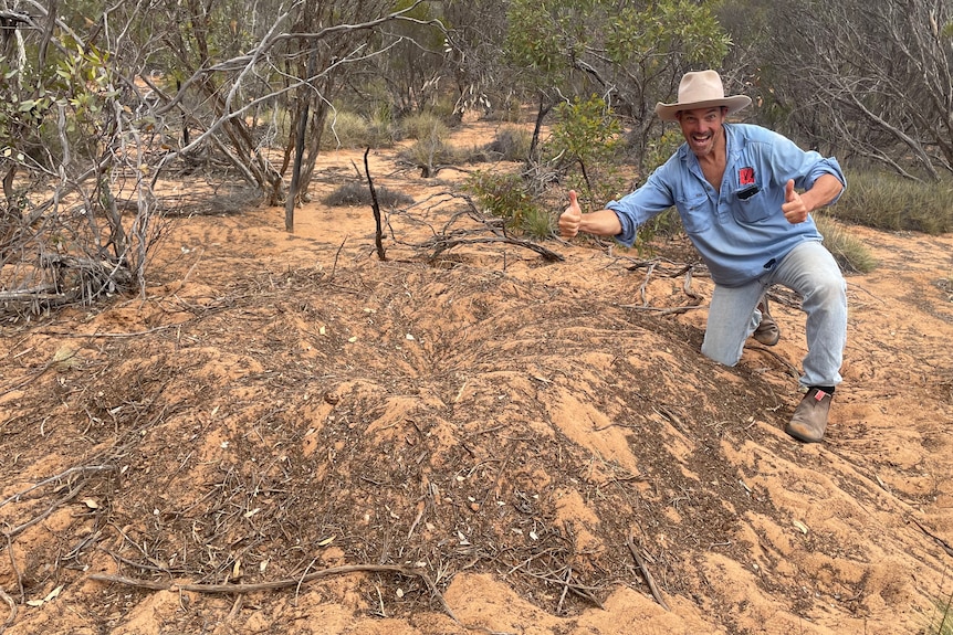Man kneeling next to dirt mound in bush smiling with thumbs up