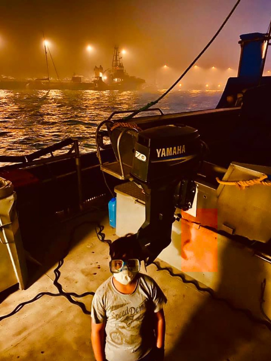 Boy in mask on boat as bushfire threatens community on land, pictured in story about children and bushfire trauma