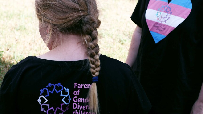 Photo from behind of a girl with a long blond braid, wearing a t-shirt that says 'Parents of gender diverse children'