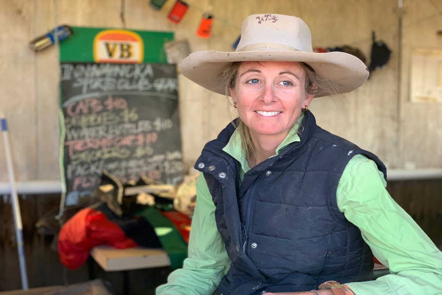 A woman in a green shirt and vest looks off camera.  She is wearing an old cowboy hat.