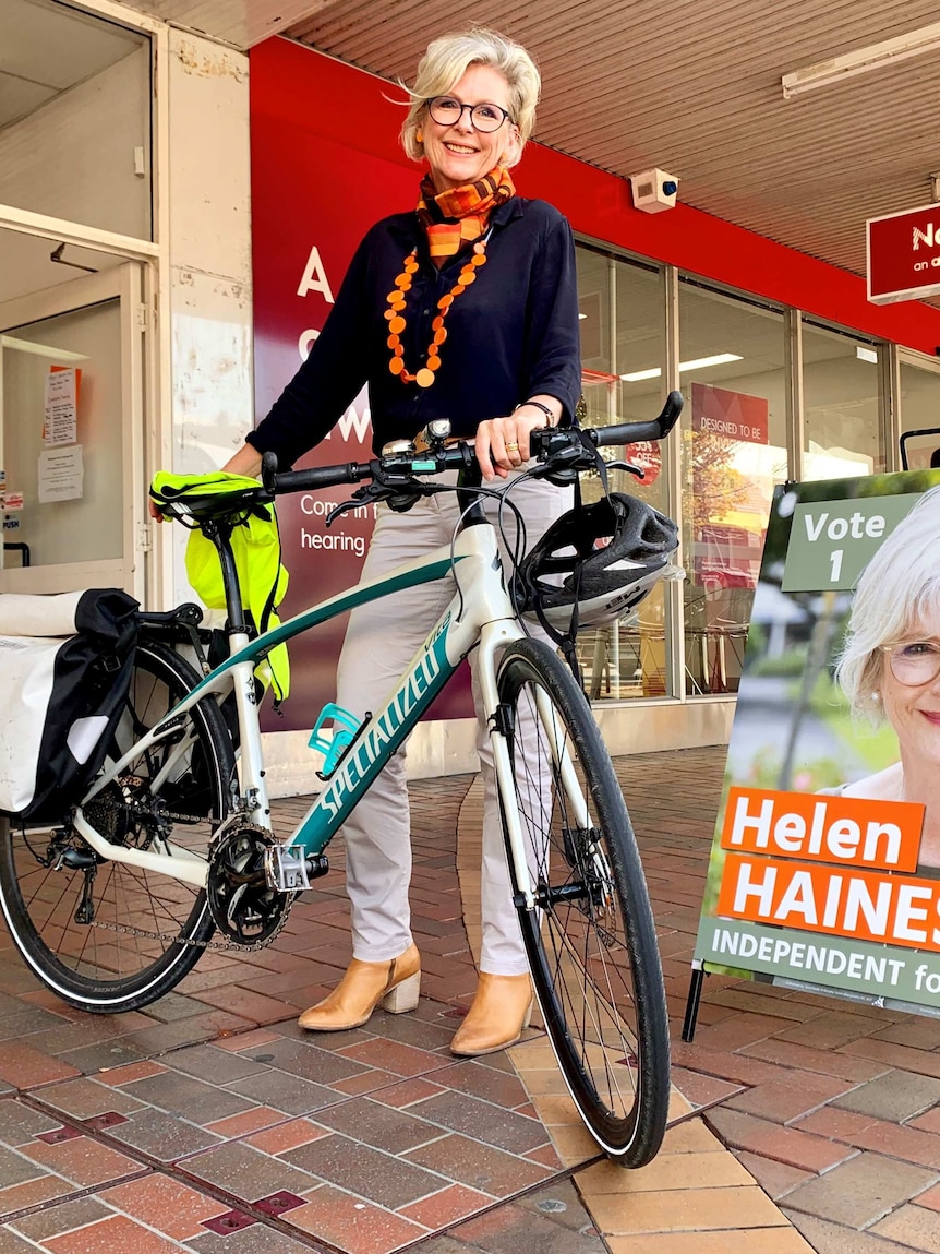 Helen Haines stands holding her bicycle, in front of signage outside her campaign office.