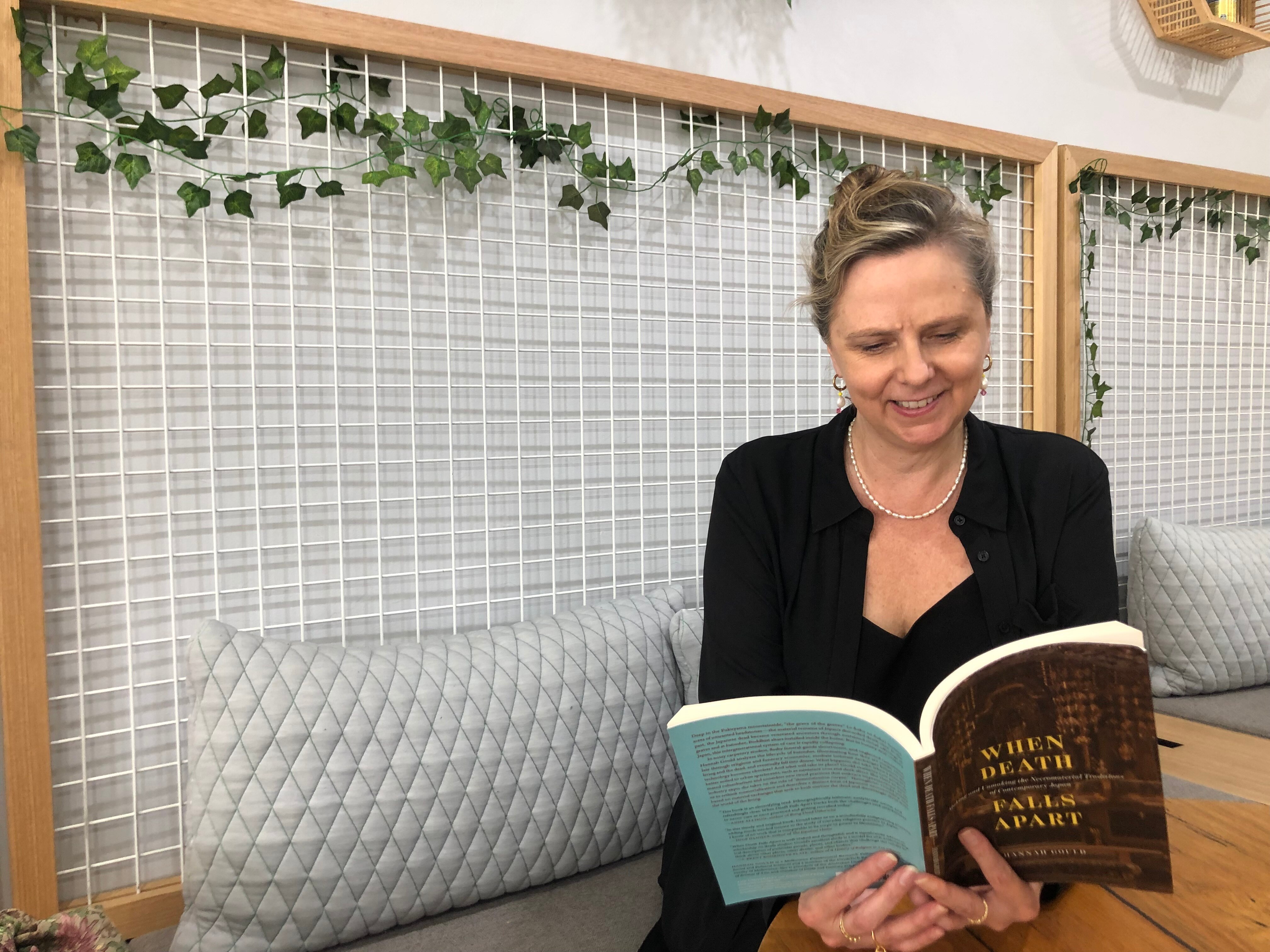 A woman with fair hair sits on a bench seat reading a book