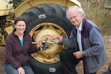 A man and woman squatting beside a tractor wheel with a smartphone clamped to the centre of the wheel.