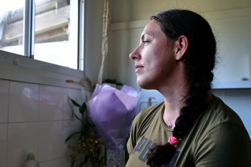 a woman stands by her kitchen sink, staring out at the window