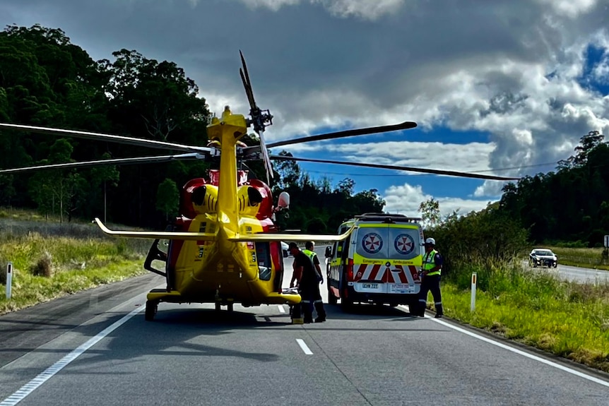 A yellow helicopter on highway next to ambulance