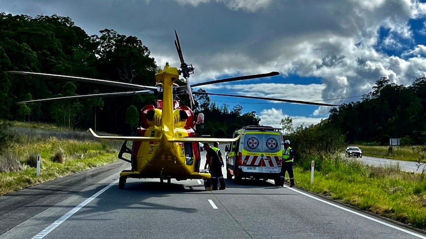 A yellow helicopter on highway next to ambulance