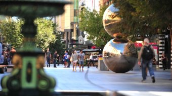 A pedestrian center with a fountain and a sculpture of two silver balls on top of each other
