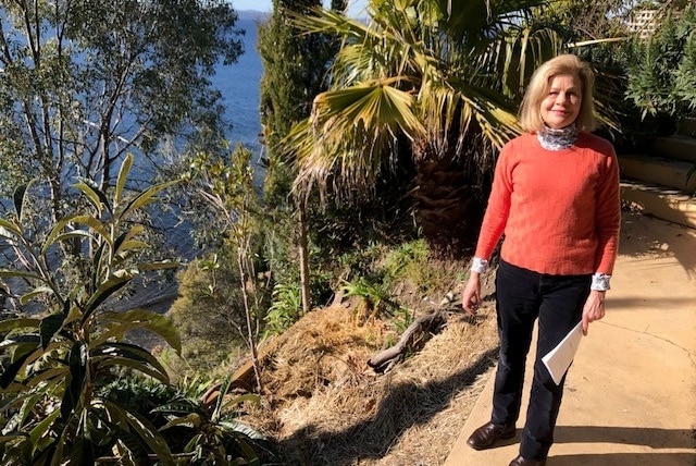 A woman wearing a bright peached-coloured top smiling in a steep garden