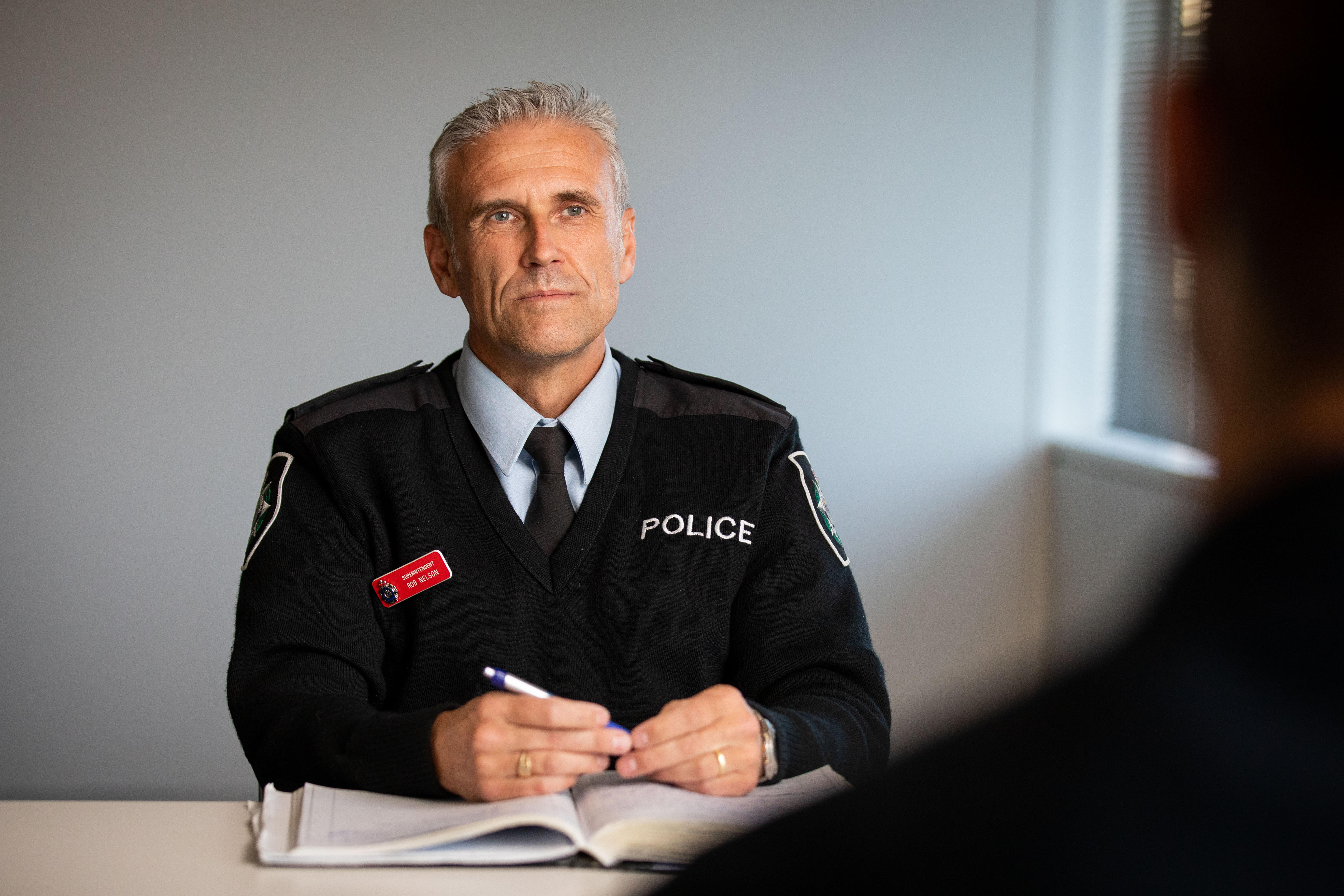 A man in a police uniform sits at a desk.